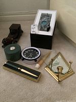 Three clocks, a wooden car model, letter opener, brass candle holder, seashell decor, spare cut glass, and a pen in a box all arranged on beige carpet.