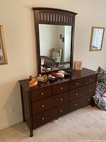 Front view of eight-drawer wood dresser with attached rectangular mirror reflecting room.
