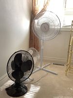 Photo showing the three fans in the lot: one black desk fan, one white desk fan, and one white standing fan near a window.