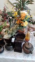 Large assortment of faux flowers, metal temple jar, and various glass vases grouped on a table