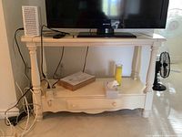 Full view of off white hall stand table with TV on top, drawer and bottom shelf visible with various items.