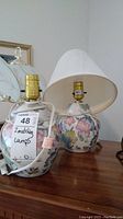 Two hand-painted Asian style ceramic table lamps on wooden surface, one with white fabric shade and one missing shade.