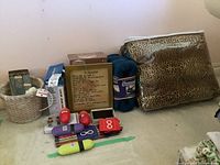 Wide view of all items placed on the floor against a wall including the leopard blanket in storage bag, blue Snuggie, suspenders, hair dryer, glass votive holder, glass tray, wallet, playing cards, and coasters.