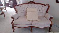 Front view of the tufted love seat with wooden frame and two cream colored pillows.