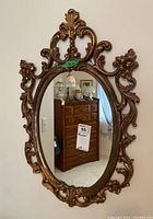 Full view of the ornate oval wall mirror with gold-colored composite frame hanging on a wall.
