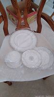 Set of Royal Doulton china pieces including teacup, saucer, bread plate, salad plate, and dinner plate arranged on a chair with original packaging box in background.