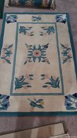Photo of the smaller rectangular decorative mat with floral designs and turquoise border on a gray carpet background.