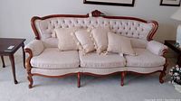 Front view of the upholstered sofa with carved wood accents and tufted back, showing the full length with pillows on seat.