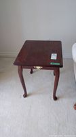 Front view of one wood side table with faux drawer front and brass handle, showing scratches on surface.