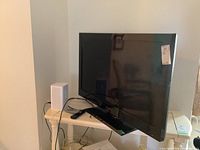 Side and front view of the black 40-inch Emerson TV placed on a white wooden table with the power cable and remote visible. No stand included.