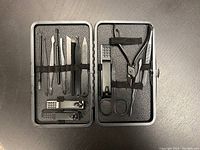 Opened black leatherette case with 16 stainless steel manicure tools held in elastic bands inside.