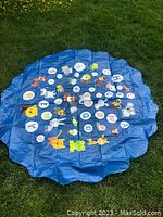 Blue inflatable water splash pool and play mat laid flat on grass, showing colorful cartoon animals and letters printed on surface, no water inside.