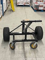 Front view of the black steel trailer dolly showing large pneumatic tires and four caster wheels on a warehouse floor.
