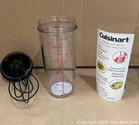 Photo showing clear plastic shaker jar with red measurement markings, detached black whisk lid, and product pamphlet.