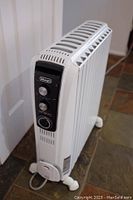 Front-angled photo of the white De’Longhi oil radiant heater showing control panel and wheels.