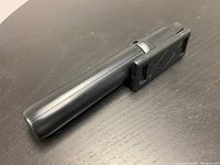 Photo of the selfie stick tripod folded to compact size, showing the black aluminum alloy handle and phone holder in collapsed position.