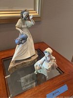 Photo showing both Lladro NAO porcelain statues side by side on a glass table under a framed picture.