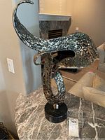 Full view of the abstract brass sculpture mounted on black granite base with a small crystal box beside it.
