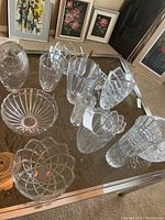 Overview photo displaying twelve plus crystal pieces including bowls and vases on a glass table.