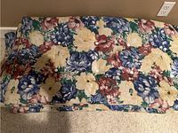 Four rectangular outdoor seating cushions with a multicolored floral pattern arranged stacked and spread out to show design and size.