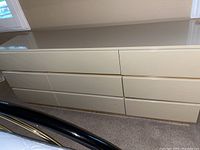White glossy dresser with 9 drawers closed, showing smooth front drawers and clean design, located near windows.