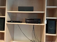 Electronics setup with Yamaha receiver and Panasonic Blu-Ray player on a wood shelf, five black speakers surrounding.
