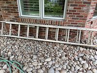 Full view of the Werner aluminum extension ladder laid horizontally on rocks outside a brick wall.