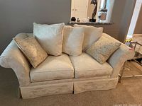 Front view of beige fabric loveseat with four cushions on carpeted floor.