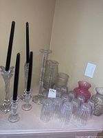 Overview of all items: twelve ribbed water glasses in front, three pairs of crystal candlesticks varying in design behind, and three vases including pink and clear etched ones.