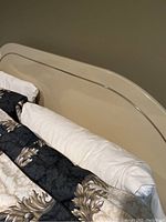 Beige headboard with chrome or metallic trim, bedding and pillows arranged on bed