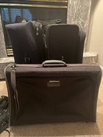 Three suitcases and one clothes bag arranged for photo, showing black and blue colors and luggage details