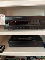Yamaha RX-V393 AV receiver top shelf, Denon CD player on middle shelf with remote, and part of a speaker on bottom shelf.