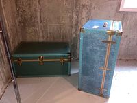 Two blue vintage trunks placed on a basement concrete floor against unfinished concrete walls, showing relative sizes and colors.