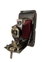 Angled front view of Kodak 1A Folding Pocket camera, showing red leather bellows, lens, and dial controls.