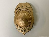 Front view of badge showing eagle crest, 'Commissioner Playground', 'City of Gloucester Incorporated 1642', central sailboat design
