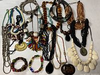 Photo of multiple costume jewelry pieces spread out on fabric surface showing a variety of necklaces and bracelets in different styles and colors.