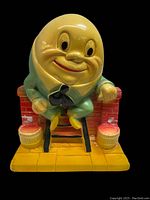Front view showing full figurine with Humpty Dumpty character sitting on a red brick wall with yellow base and barrels.
