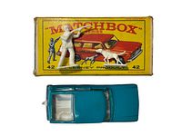 Top view of the original Matchbox Lesney Series #42 Studebaker blue toy car, white hunter figure, and white dog figure arranged on the yellow Matchbox box.