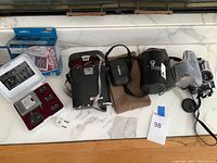 Full lot photo showing Canon cameras, Nikon binoculars, Soligor lens, and plug converter kit on marble surface