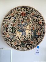 Full view of the large round ceramic plate with detailed hand painted design including floral patterns and figures on a cream background.