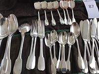Three large serving ladles, four smaller forks, four teaspoons, six sugar spoons and six dinner knives arranged on cloth.