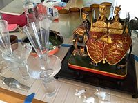 Photo showing clear glass stemware pieces, ceramic ocean bowl, small pottery pieces, silver fish item and Asian elephant statue on black base