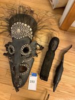 Overall view of mask and two small wood figures arranged on a hardwood floor