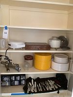 Shelving unit with electric juicer, plastic dishes, large corkscrew, and flatware sets visible