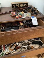 Image showing dresser with drawer opened revealing assorted jewelry pieces including beaded necklaces and assorted jewelry and accessories scattered on top and inside drawer.
