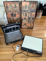Two wooden religious panels, black leather briefcase open, electric tracing light box on hardwood floor