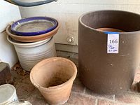 Overview of assorted pots including large brown plastic pot, small terracotta pot, cream patterned ceramic planter and stacked saucers