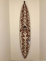 Full view of the elongated wooden shield hung on a wall, showing overall shape and design