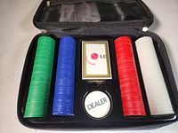 Open poker chip set showing four stacks of poker chips in green, blue, red, and white colors, one deck of playing cards, and a dealer marker in a black case.