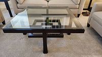 Square coffee table with glass top and dark wood base, detailed front view.